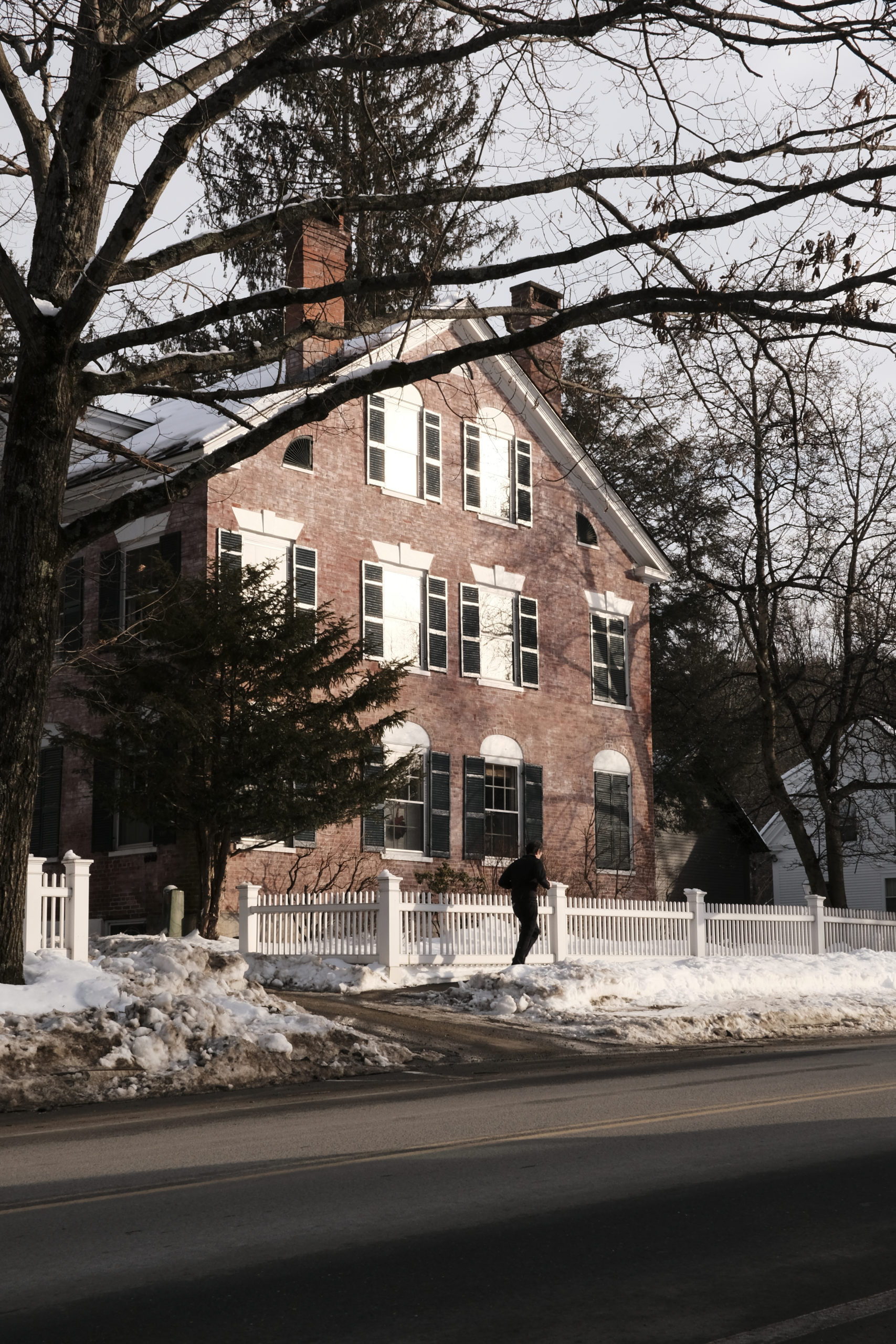 Person running in front of brick house with the sun reflected in the windows.